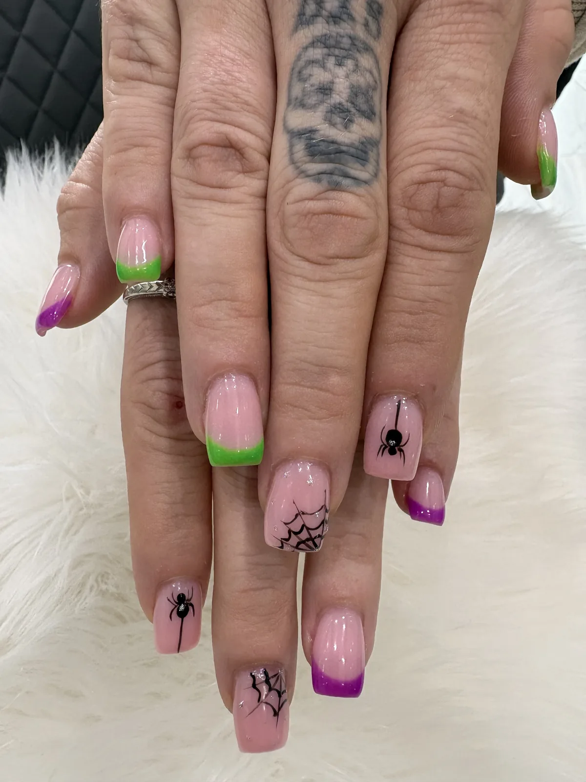 Close-up of square pink nails with purple and green tips, black spiders and spiderweb accents